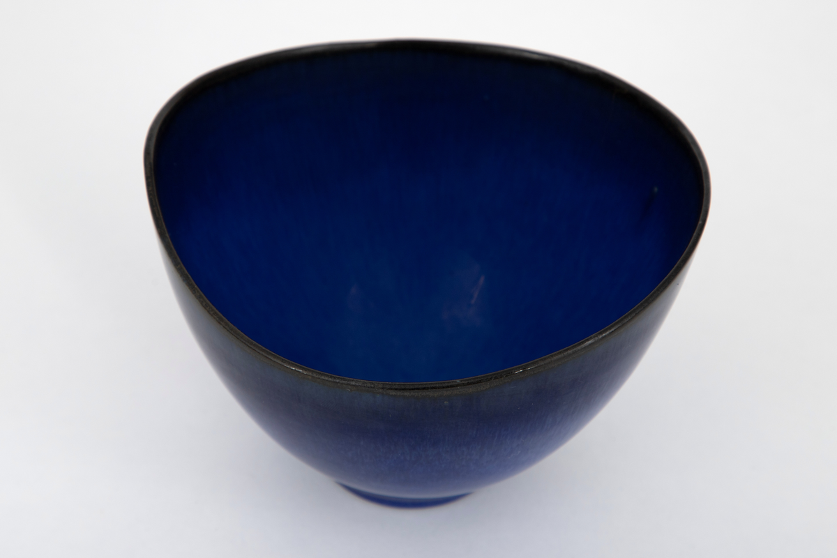 Skål i steingods, oval form med noe skjevt oppsvunget munningsrand i begge ender. Dekket med blank glasur i skiftende nyanser av blått, lysere blå mot bunnen og dypblå nærmere munningsranden.