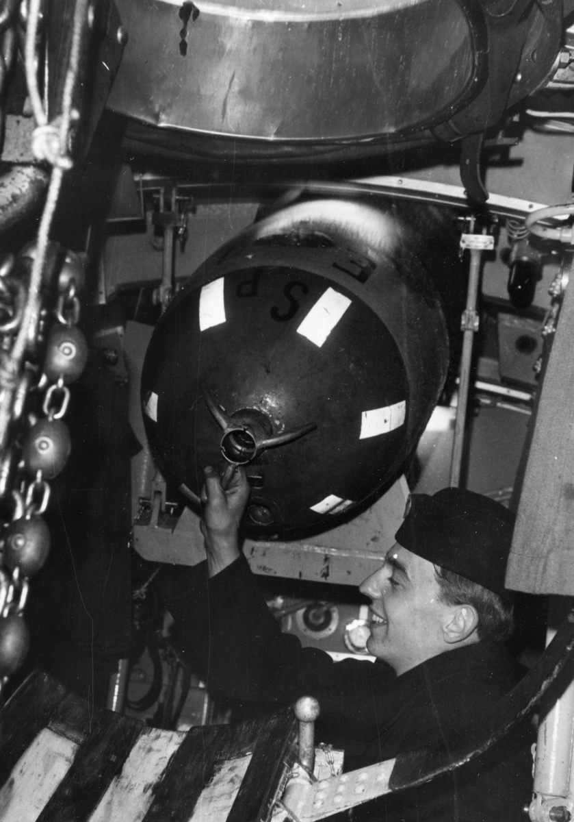 Torped strax ovan vattenytan i en lyftanordning. Det sitter linor längst fram och längst bak på torpeden, runt dess mitt sitter ännu en lina.