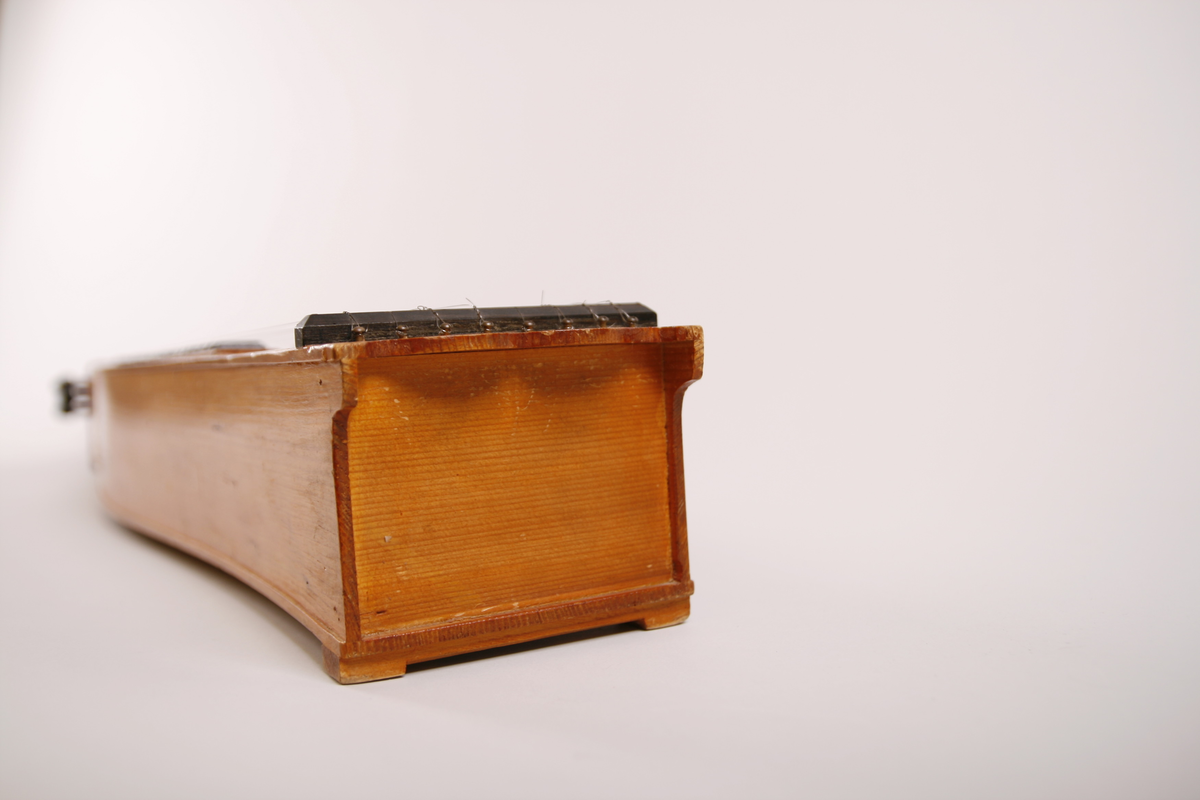 Lang, smal, buket korpus av gran. Skruekasse og hode i ett stykke. Hode i form av en snekke der profilene er dekorert med bronsemaling. Sortmalte stemmeskruer med perlemorsøye på kanten av hodet. Rundt lydhull. Tusjborder langs lokkanten og rundt lydhullet, samt blomstreranke i tusj nederst på lokket.
1 melodistreng og 7 resonansstrenger. Under melodistrengen 14 pålimte noter i ibenholt (spor etter fler noter enten flyttet eler fjærnet). Stopper mangler. 3 pyamider mangler. Strengeleder i form av skruer med insaget hakk. 
Strengene er festet med anhengsskruer direkte bak stolen på lokket. Skruene (8 st) er festet gjennom lokket i nedre sarg
Instrumentet er usignert.