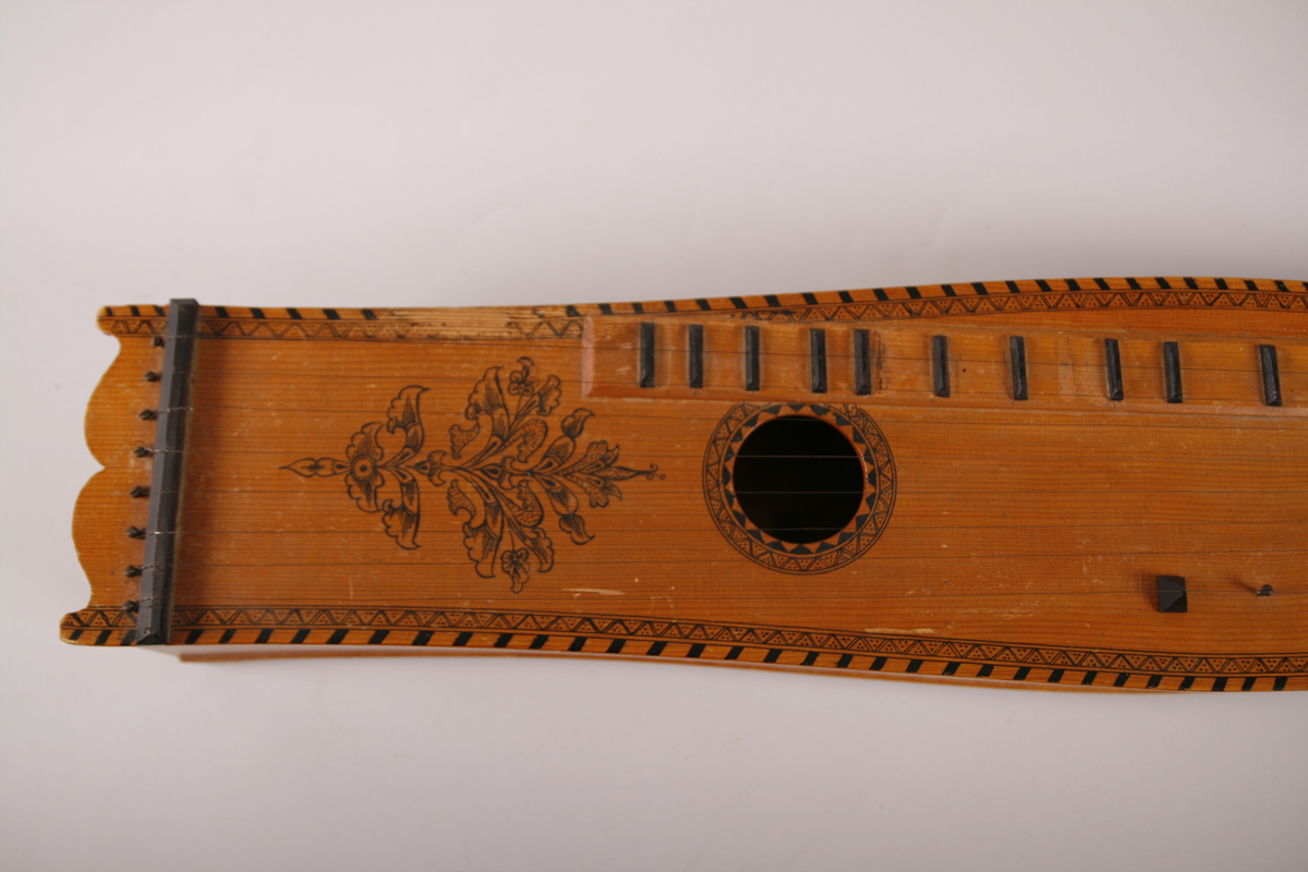 Lang, smal, buket korpus av gran. Skruekasse og hode i ett stykke. Hode i form av en snekke der profilene er dekorert med bronsemaling. Sortmalte stemmeskruer med perlemorsøye på kanten av hodet. Rundt lydhull. Tusjborder langs lokkanten og rundt lydhullet, samt blomstreranke i tusj nederst på lokket.
1 melodistreng og 7 resonansstrenger. Under melodistrengen 14 pålimte noter i ibenholt (spor etter fler noter enten flyttet eler fjærnet). Stopper mangler. 3 pyamider mangler. Strengeleder i form av skruer med insaget hakk. 
Strengene er festet med anhengsskruer direkte bak stolen på lokket. Skruene (8 st) er festet gjennom lokket i nedre sarg
Instrumentet er usignert.