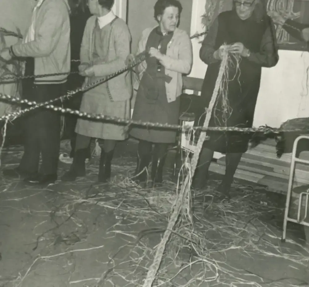 To kvinner i et rom som fletter et langt rep.