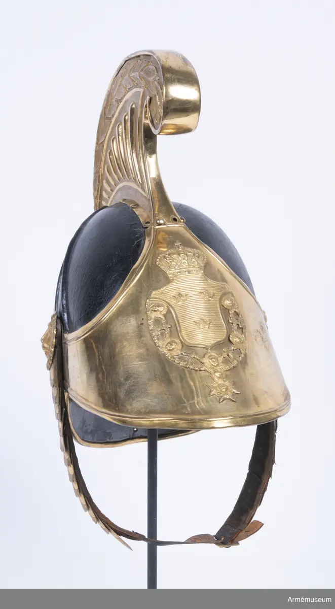Kask med förgylld mässingskam.

Kasken är tillverkad av svartlackat tjockt läder som har pressats och formats till en hjälm.
Den består av två halvdelar med söm på mitten som döljs på utsidan av en mässingskam som löper från pannan till nacken. Kammen är dekorerad med lagerblad längst upp och avslutas i ett volut fram. Den sitter ihop med framskärmen/vapenplåten. Från kullen och ner löper två svarta ribbor på varje sida, troligen med stål inuti.
Kasken har välvd mässingsskärm fram i vilken den separat stansade vapenplåten är fastsatt, och nackskydd bak kantad med mässingslist. Vapenplåten består av vapensköld med tre kronor (Lilla Riksvapnet) inom en ordenskedja för Serafimerorden. Kring hjälmen i nacken löper ett beslag av mässing i form av en stiliserad lagerkrans med bär.
Hakremmen är klädd med flerflikiga dekorerade mässingsfjäll som överlappar varandra i gradvis minskande storlek, och är fäst i varje sida under en stor lejonmaskaron av mässing. Remmen är fodrad med svart sammet, och spänns ihop mitt fram med ett litet mässingsspänne. Flera fjäll saknas i vänster remhalva.
Kaskinredningen är av mörkbrunt skinn, fastsatt längs med Kaskens innerkant och bestående av klippta tungor med en mässingsöljettl i varje rundning, genom vilka kunde löpa ett band eller en rem som kunde justeras efter huvudstorlek.

Kammen saknar fäste för tagelliggare.
