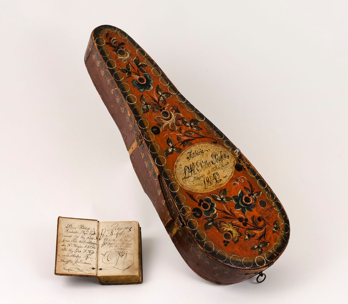 Fiollåda, troligen tillverkad och målad av Larshans Per Persson (1820-1879).

Lådans sarg i tunt svep, fästat med metallstift. Lockets två gångjärn i koppar är båda trasiga. Sarg och botten sammanfogade med träplugg. Vitmålad insida, nött. Lockets undersida rödmålad med text: "LHPPS 18 7/3 42". Stämplade vita punktcirklar på sarg och lock. Lockets ovansida med röd bottenfärg och sirlig blomster i flera färger. Målad ljus oval med texten: "Tillhörig L.H. Petter PersSon 18 7/3 42".
Underliggande tidigare blomstermåleri synligt.