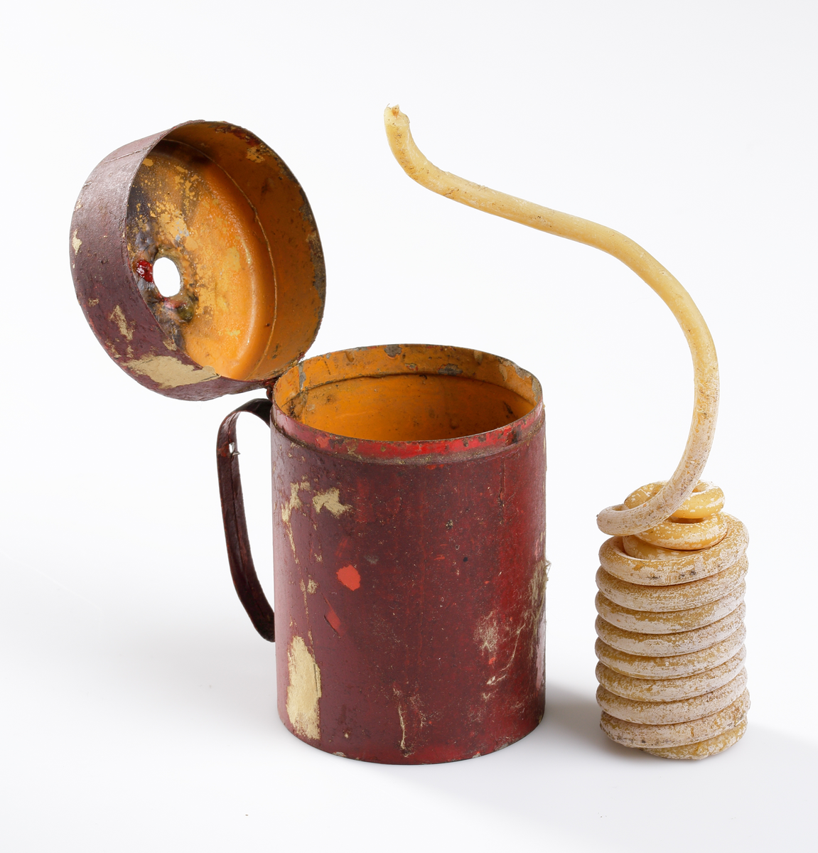 Vaxstapelhållare med vaxstapel. Cylinderformad burk av plåt, med lock och vid ena sidan ett handtag. I locket ett hål för vaxstapeln. Invändigt målad gul, utvändigt röd, botten svart. inuti burken en sprialformad vaxstapel.

Inskrivet i huvudkatalog 1952.