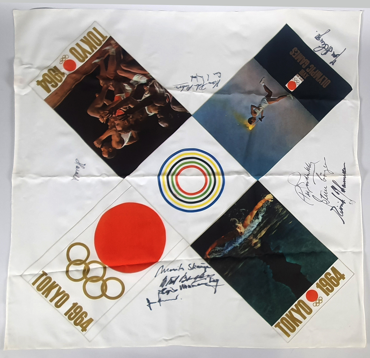 Hvitt, kvadratisk silkesjal, med emblem fra sommer-OL i Tokyo 1964. Påtrykte bilder av en mann med fakkel, en som svømmer og flere personer som løper. I midten fem sirkler innenfor hverandre i de olympiske fargene. Silketørklet er signert av de norske seilerne.