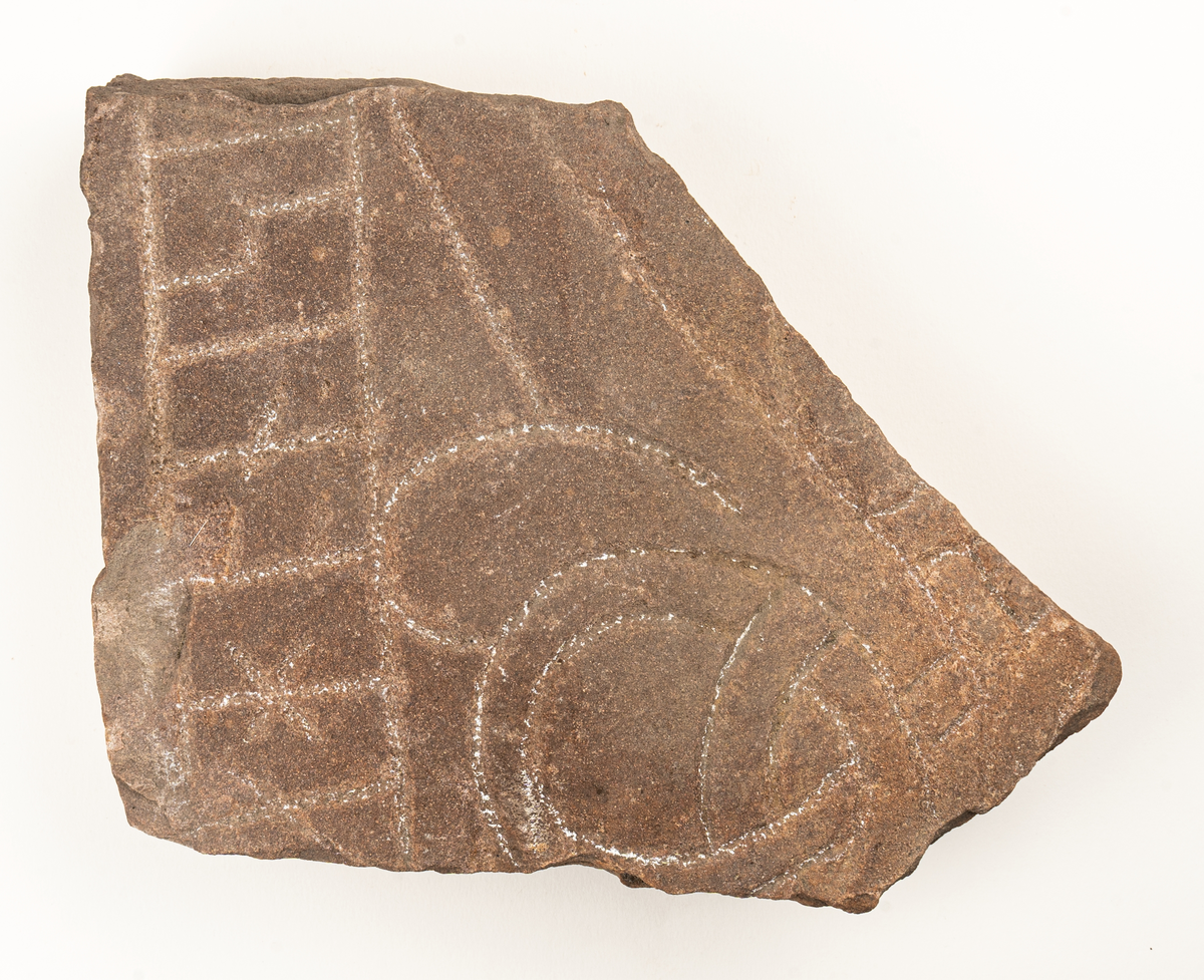 Runstensfragment av mörkgrå gävlesandsten. På ena flatsidan runband med bokstäverna : ahonisi. Därunder delar av slingornament. Runsten Gs 18, del D.
Ristad av Åsmund Kåresson i mitten av 1000-talet.