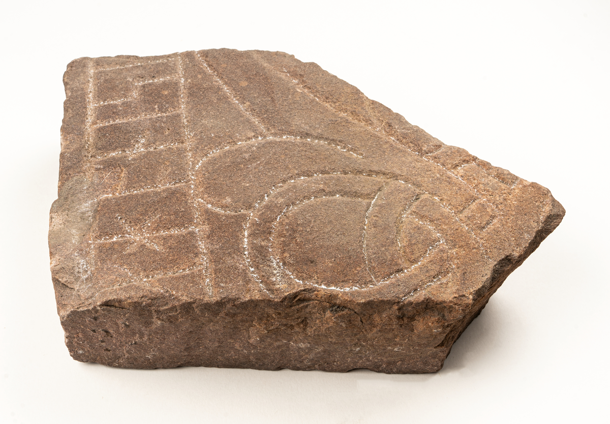 Runstensfragment av mörkgrå gävlesandsten. På ena flatsidan runband med bokstäverna : ahonisi. Därunder delar av slingornament. Runsten Gs 18, del D.
Ristad av Åsmund Kåresson i mitten av 1000-talet.