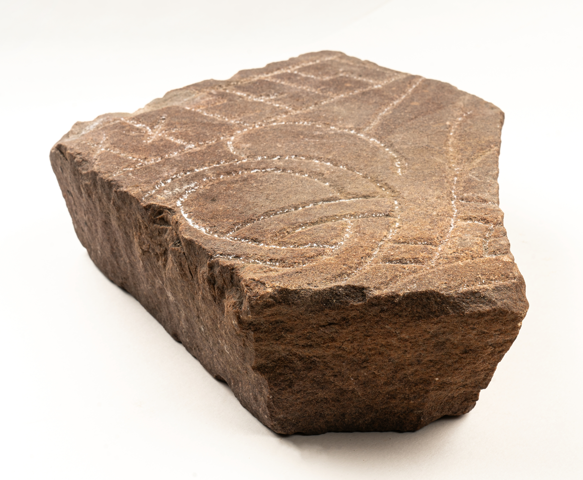 Runstensfragment av mörkgrå gävlesandsten. På ena flatsidan runband med bokstäverna : ahonisi. Därunder delar av slingornament. Runsten Gs 18, del D.
Ristad av Åsmund Kåresson i mitten av 1000-talet.