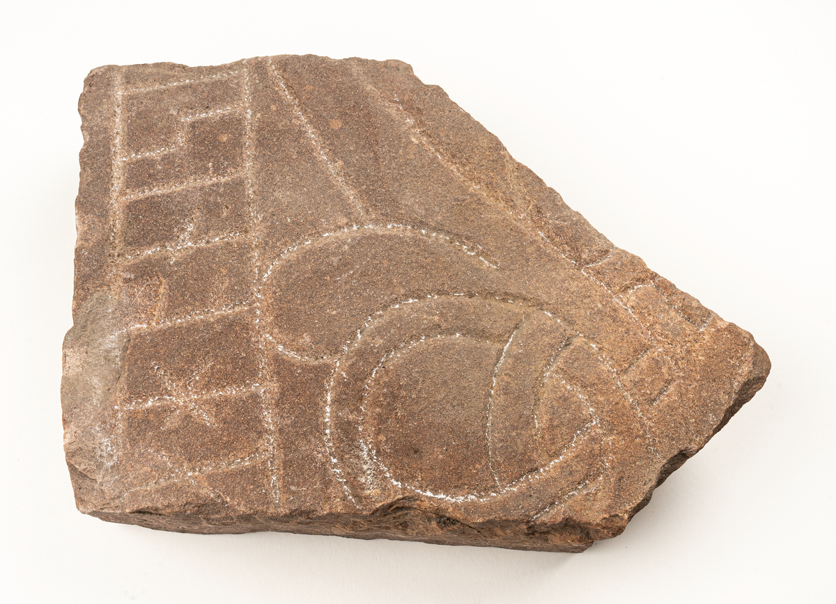 Runstensfragment av mörkgrå gävlesandsten. På ena flatsidan runband med bokstäverna : ahonisi. Därunder delar av slingornament. Runsten Gs 18, del D.
Ristad av Åsmund Kåresson i mitten av 1000-talet.