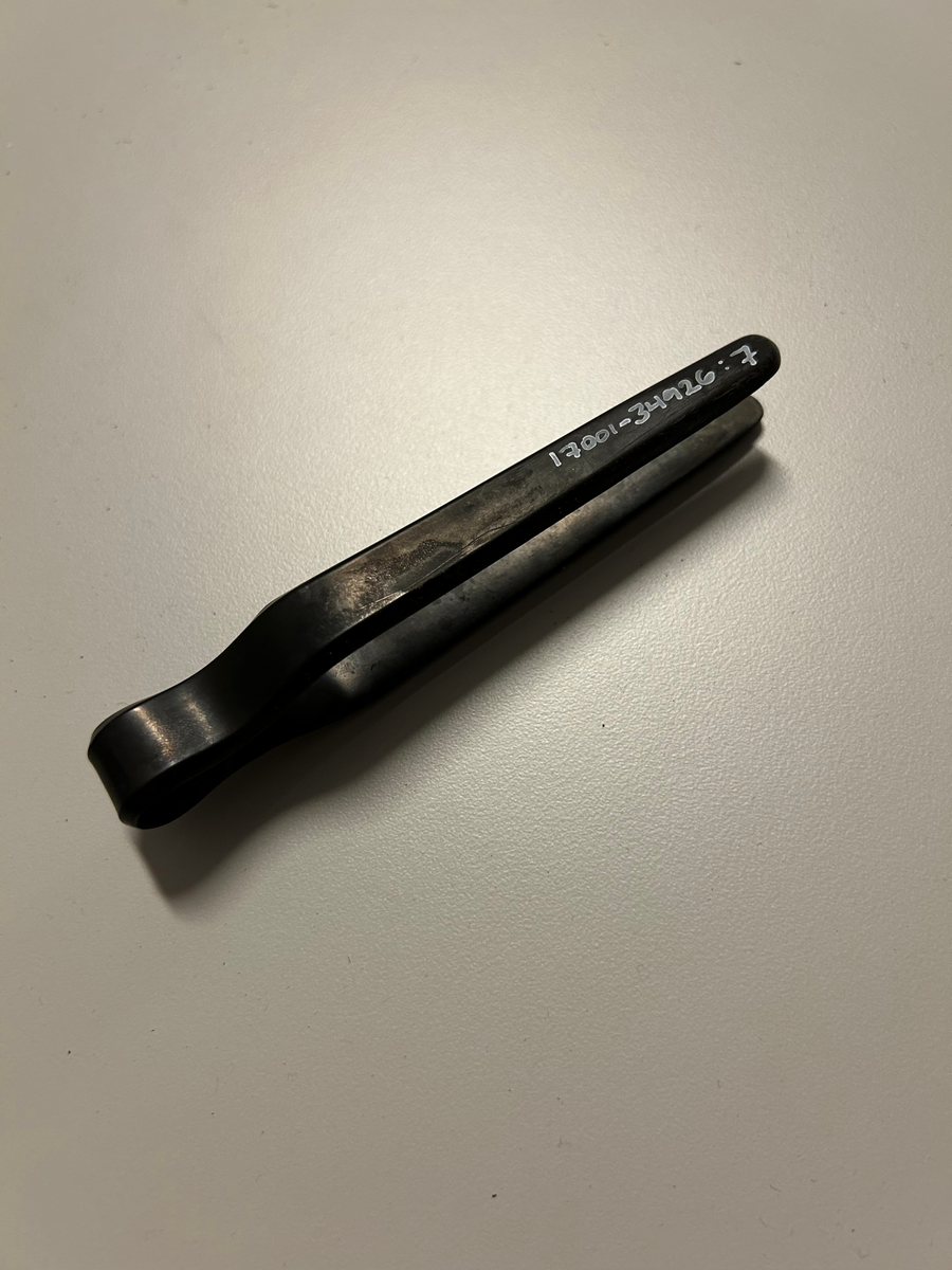 Pincettformad av svart plast med tångfunktion, genom två tenar som sitter ihop i ena ändarna och kläms ihop över det objekt man vill plocka upp.