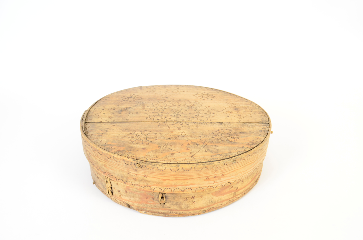 Gran. Sirkulær. Bunn og topp består av bord med spor langs kanten. Sidene, både i eske og lokk, utgjøres av bøyd spon, sydd sammen med tæger. Lokket er noe videre enn esken. Enkel sviornamentikk på innsiden av bunn og lokk, under bunnen og på sidene, rikere ornamentikk på lokkets overside. Sentralt sirkulært motiv, omgitt av fire kvadrater og fire rosetter. Buebord langs alle kanter.