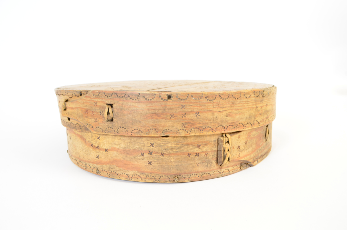 Gran. Sirkulær. Bunn og topp består av bord med spor langs kanten. Sidene, både i eske og lokk, utgjøres av bøyd spon, sydd sammen med tæger. Lokket er noe videre enn esken. Enkel sviornamentikk på innsiden av bunn og lokk, under bunnen og på sidene, rikere ornamentikk på lokkets overside. Sentralt sirkulært motiv, omgitt av fire kvadrater og fire rosetter. Buebord langs alle kanter.