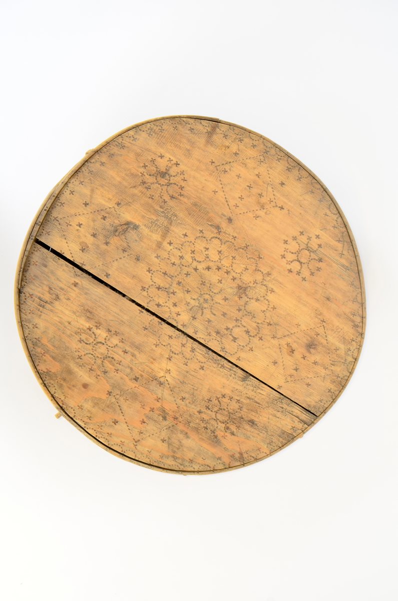 Gran. Sirkulær. Bunn og topp består av bord med spor langs kanten. Sidene, både i eske og lokk, utgjøres av bøyd spon, sydd sammen med tæger. Lokket er noe videre enn esken. Enkel sviornamentikk på innsiden av bunn og lokk, under bunnen og på sidene, rikere ornamentikk på lokkets overside. Sentralt sirkulært motiv, omgitt av fire kvadrater og fire rosetter. Buebord langs alle kanter.