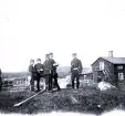 Foto av militärer poserande framför en stuga med träd och gärdsgård i bakgrunden. Text i album: 