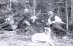 Foto av två män och två hundar som tar en vila i vad som verkar vara ett skogsparti.