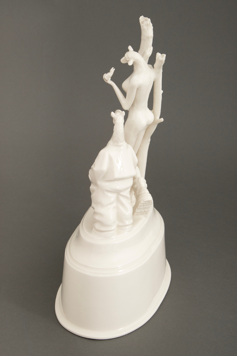 Objekt i hvitglasert porselen. På oval, hul sokkel står flere stiliserte figurer. Ytterst til høyre en figur med hestehode ikledd dress. I midten en figur med kvinnekropp og sauehode, kledd i kraftige støvler og med en avkuttet arm i ene hånden. Foran en mindre figur med hønsehode og bare en arm, vendt med ryggen mot. Ytterst til venstre to døde trær.