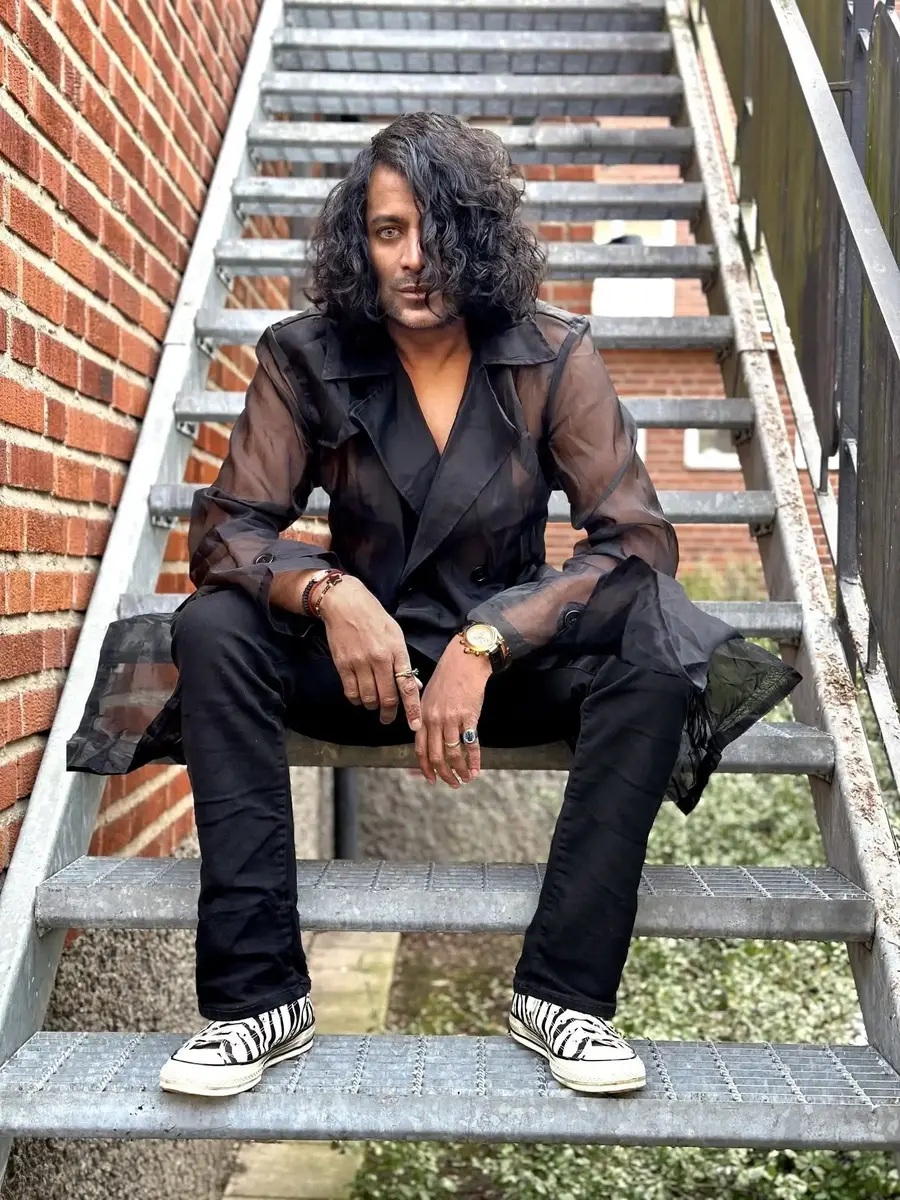 Man med långt mörkt hår sitter i en trappa med tegelvägg i bakgrunden.