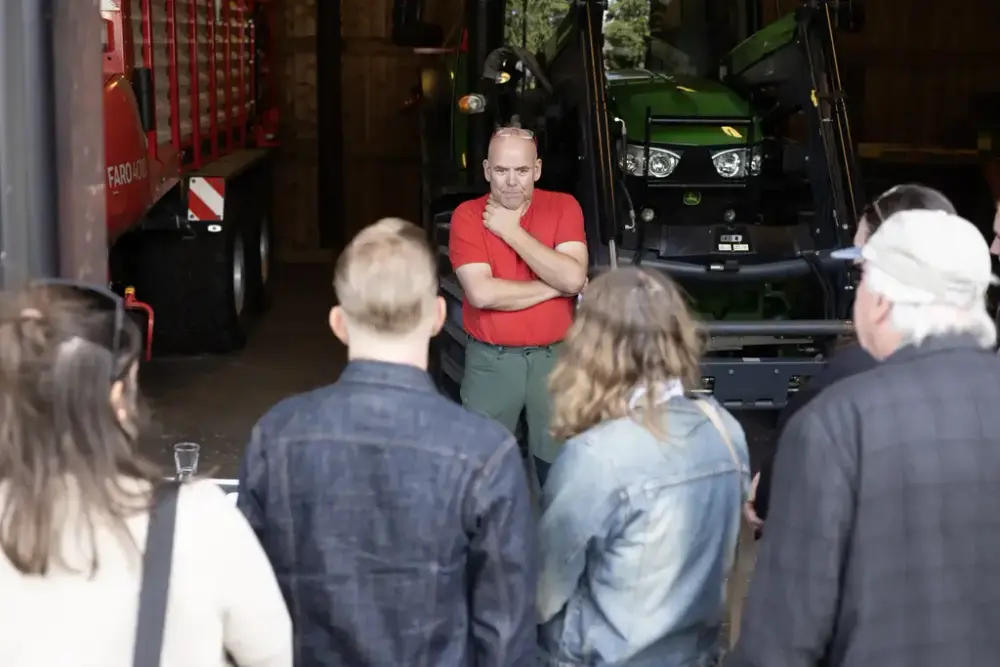 En gruppe mennesker hører på en mann snakke. Han står foran en traktor. 