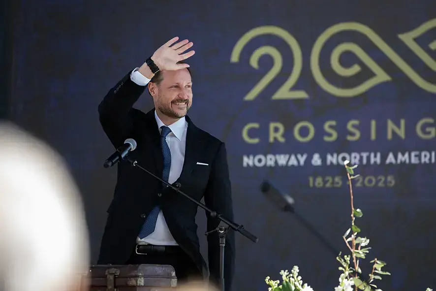 En mann i dress som vinker. Crossings 200-logo i bakgrunnen.