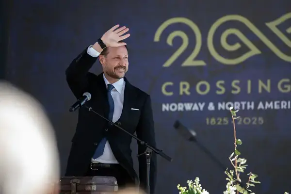 En mann i dress som vinker. Crossings 200-logo i bakgrunnen.