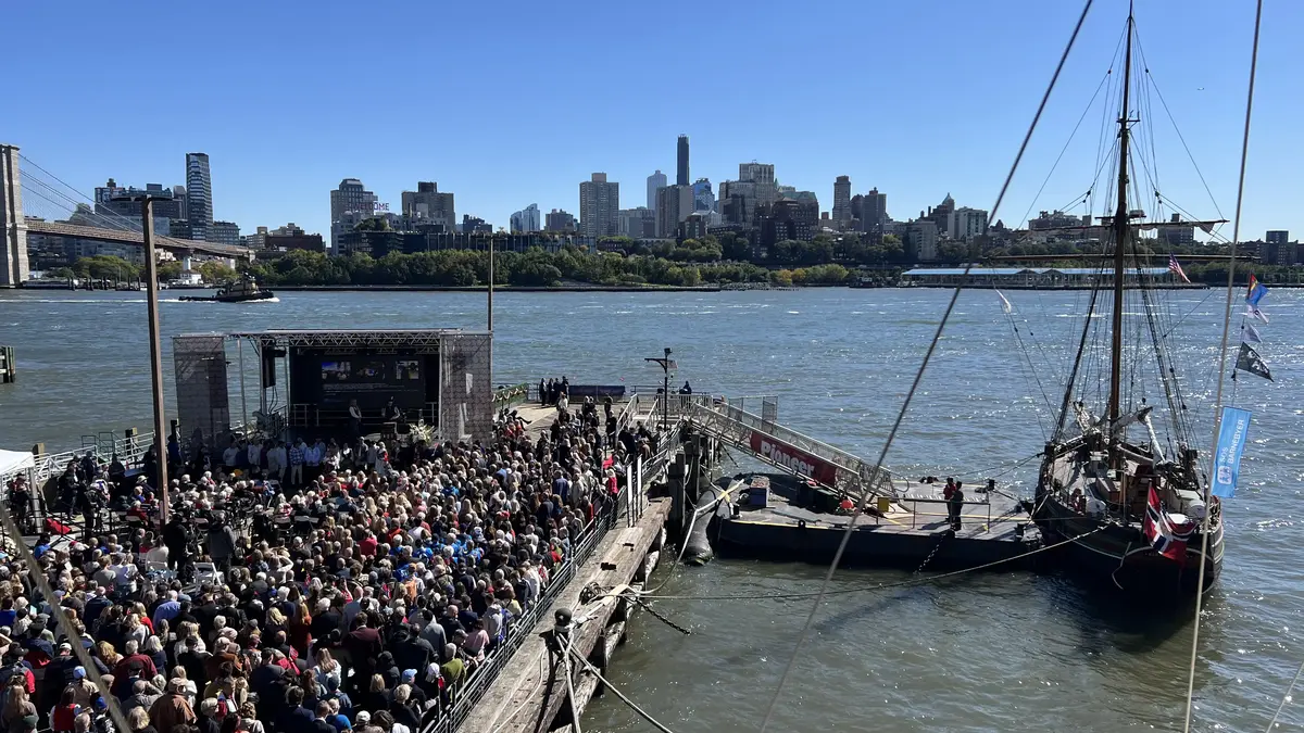 En kai full av mennesker, med en seilbåt liggende til kai.