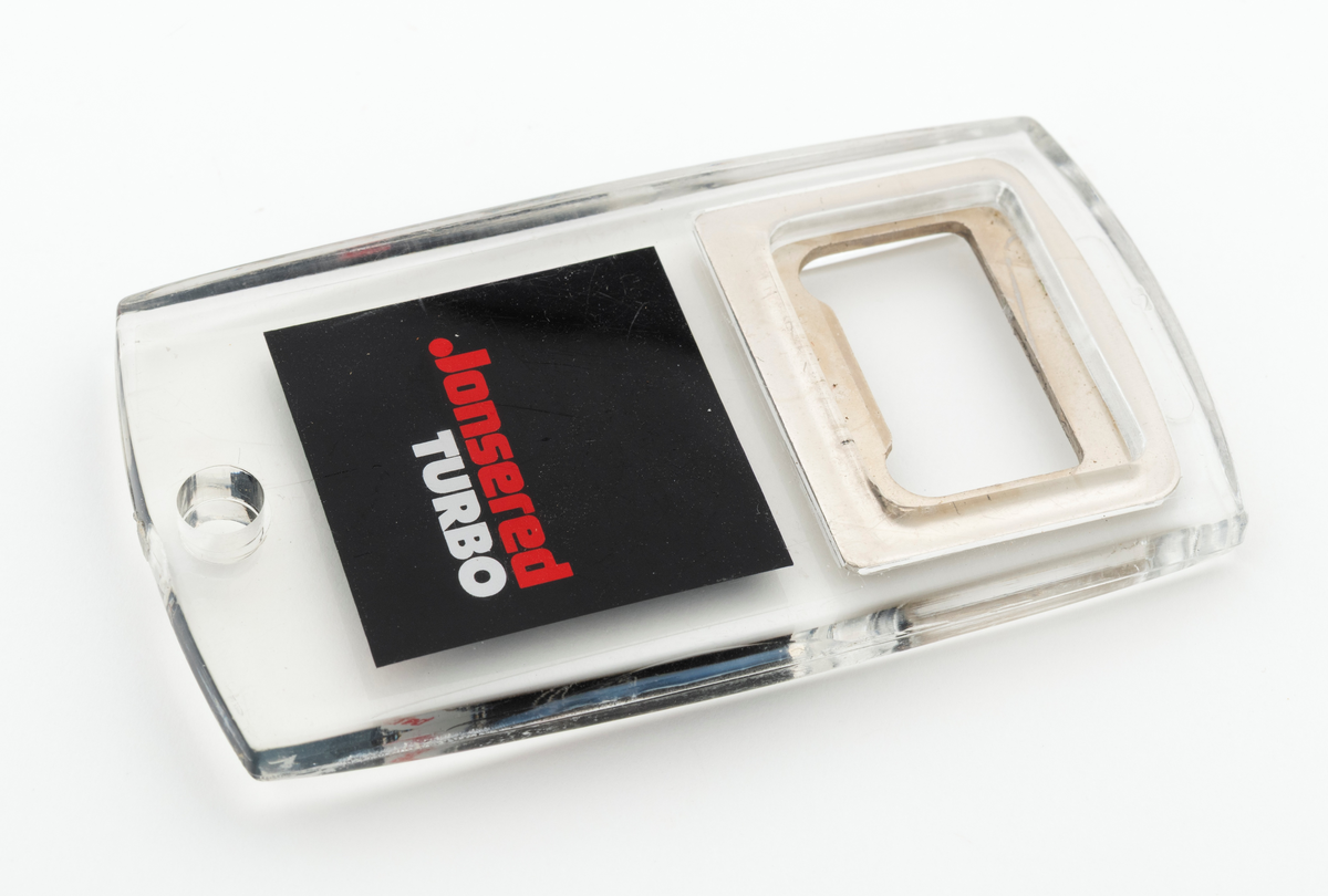 En tilnærmet rektangulær flaskeåpner som hovedsakelig er utført i støpt plast, antatt pleksiglass, med metalltann og påtrykt dekor. Metalltanna, som er støpt inni plasten/pleksiglasset har en rektangulær form. Metalltanna har en "lysåpning" som er cirka 2,6 centimeter lang og 1,4 centimeter bred. Nederst på flaskeåpeneren er det et lite hull slik at den kan henges opp eller festes til en nøkkelreing. 

Under metalltanna er det trykt et bilde av en Jonsered motorsag på den en siden og teksten Jonsered Turbo på den andre siden. Det antas at motorsagmodellen som er avbildet på flaskeåpnerens ene side skal forestille Jonsereds sagmodell 2051 Turbo, men det er ikke bekreftet. 

Flaskeåpneren er en reklameartikkel, et profileringsprodukt, for motorsagmerket Jonsered. Sagmodellen Jonsered 2051 Turbo ble lansert i 1988 og produsert til 1993. Det antas derfor at reklameartikkelen, pofileringsproduktet, ble lansert når disse sagene kom på markedet i 1988.