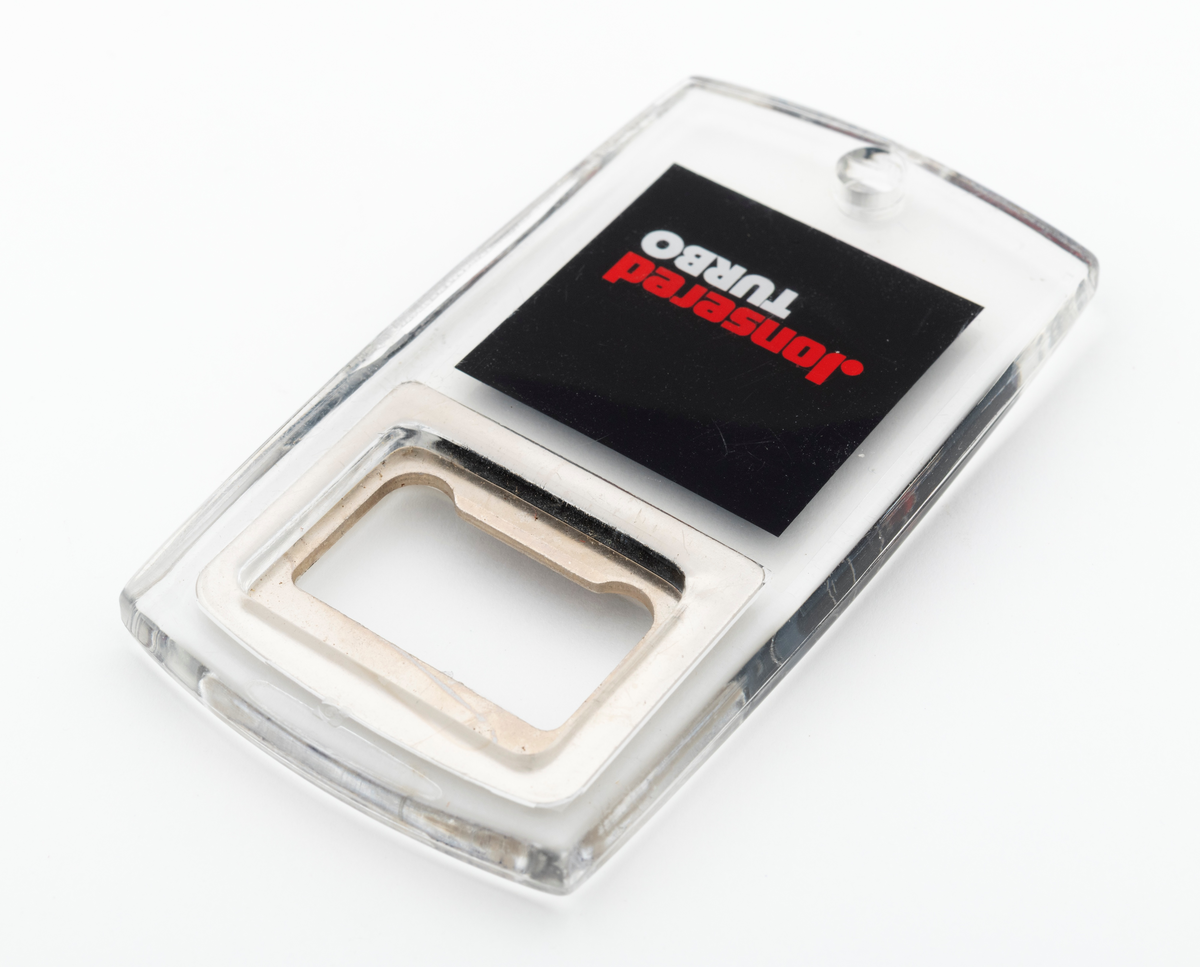 En tilnærmet rektangulær flaskeåpner som hovedsakelig er utført i støpt plast, antatt pleksiglass, med metalltann og påtrykt dekor. Metalltanna, som er støpt inni plasten/pleksiglasset har en rektangulær form. Metalltanna har en "lysåpning" som er cirka 2,6 centimeter lang og 1,4 centimeter bred. Nederst på flaskeåpeneren er det et lite hull slik at den kan henges opp eller festes til en nøkkelreing. 

Under metalltanna er det trykt et bilde av en Jonsered motorsag på den en siden og teksten Jonsered Turbo på den andre siden. Det antas at motorsagmodellen som er avbildet på flaskeåpnerens ene side skal forestille Jonsereds sagmodell 2051 Turbo, men det er ikke bekreftet. 

Flaskeåpneren er en reklameartikkel, et profileringsprodukt, for motorsagmerket Jonsered. Sagmodellen Jonsered 2051 Turbo ble lansert i 1988 og produsert til 1993. Det antas derfor at reklameartikkelen, pofileringsproduktet, ble lansert når disse sagene kom på markedet i 1988.