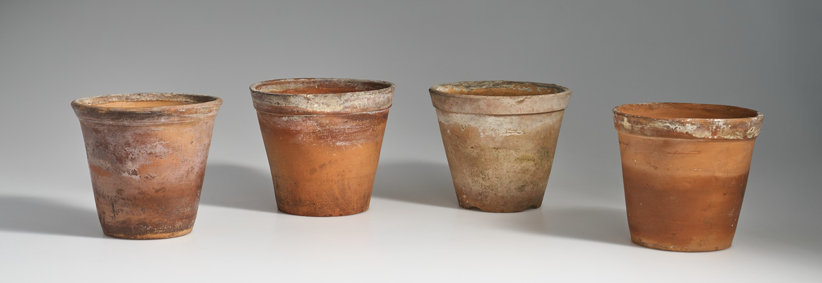 7 blomsterpotter i brent leire. Terrakottapotter med hull under i ca. lik størrelse. Ingen av pottene har jevnt fargemønster, men er alle preget av bruk. 
Pottene 01, 03, 05, 06 og 07, har en liten kant under som danner bunnen av potten, med en flat fordypning under.
Potte 02, har tynnere kant under som ikke er hel, men består av 4 kanter ovenfor hverandre, den er noe lysere i fargen og er markert med tallet "14" under.
Potte 04 har ingen kant under, men har en flat bunn.
Potte 06 har sprekkdannelse under på den ene siden, ovenfor dreneringshullet.