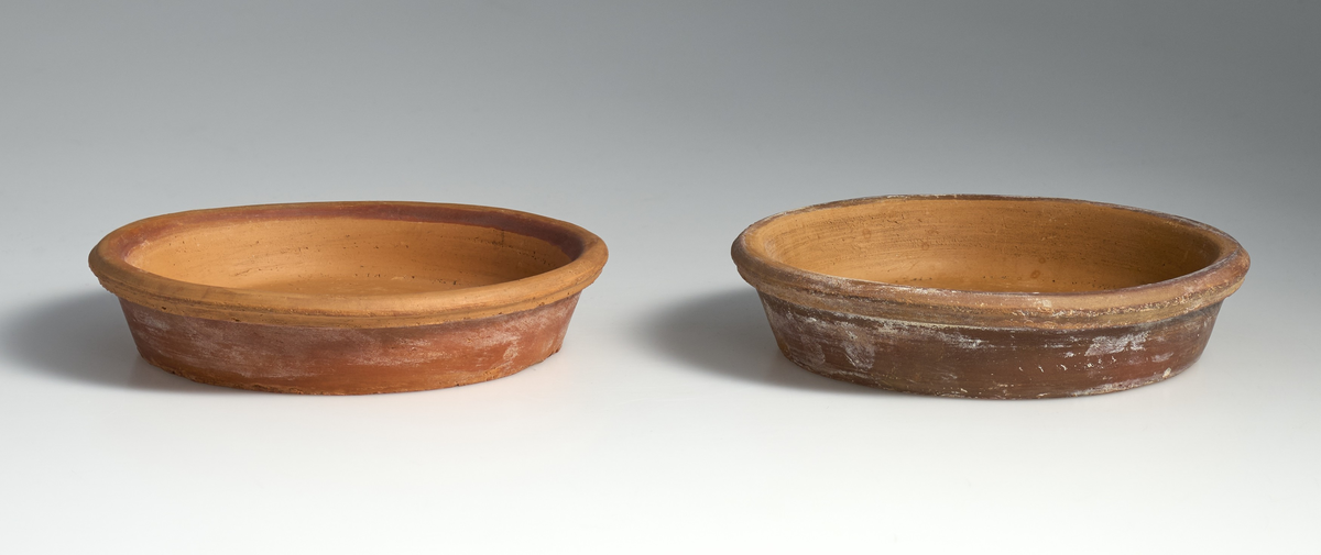 2 fat til blomsterpotter i brent leire. Terrakottafat med sirkulær og tilnærmet flat bunn, med kanter som skråner jevnt opp og utover. Øverste del av kanten rundt er avrundet og strekker seg utover kanten til fatet. Ingen av fatene har jevnt fargemønster, men er alle preget av bruk. Fatet markert med 01 er noe lysere og mer tilnærmet oransje i fargen enn 02. Fatet markert med 02  har noe gråere skjær i fargen.