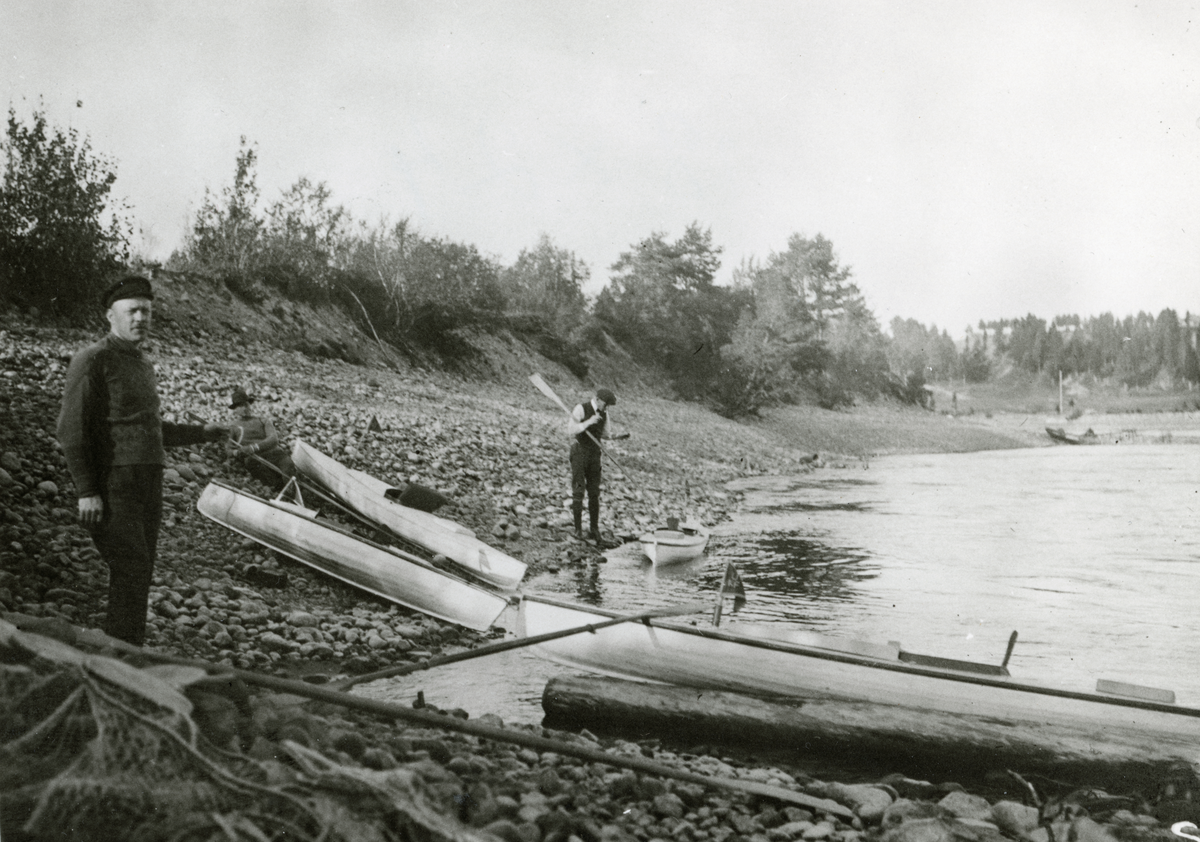 Kanotutfärd. Två män vid paddelkanoter uppdragna på strand.