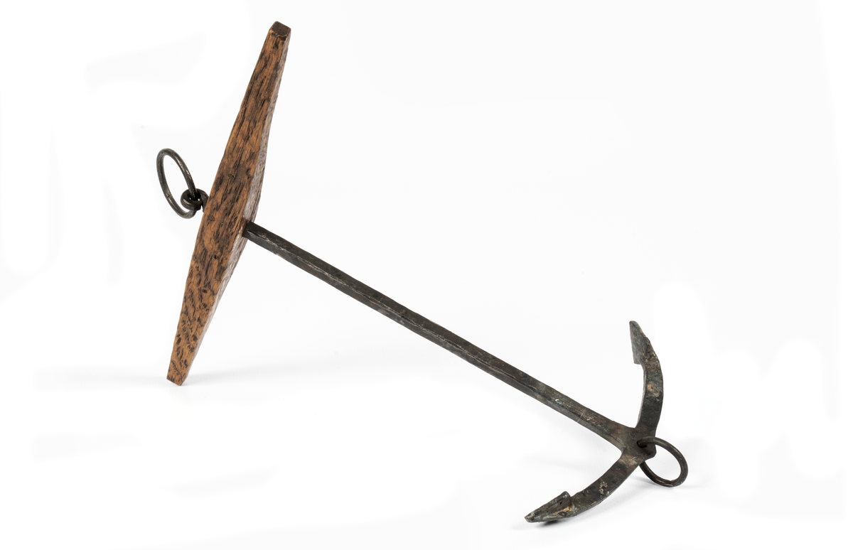 Modell av stockankare av järn med fyrkantig lägg, platta armar, små trapetsformade flyn (elsvetsade). Liten ring i kronan. Stock av ek med liten påspikad kloss.