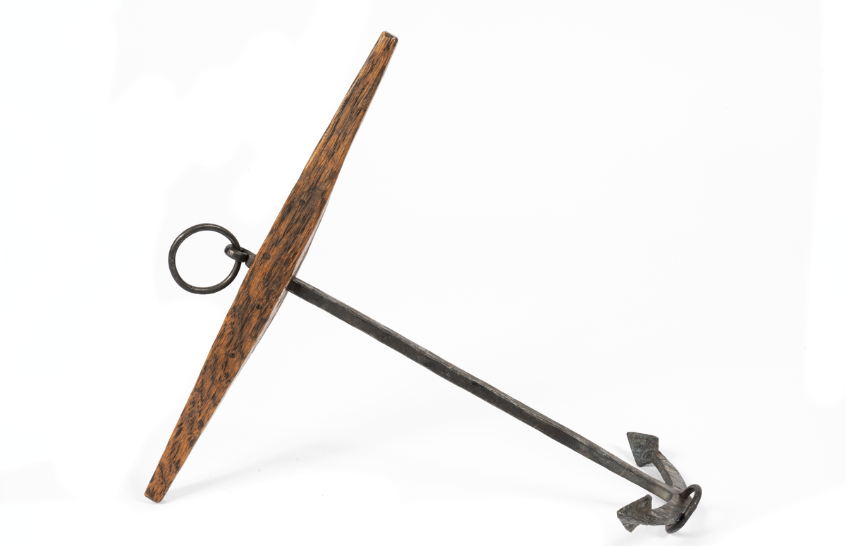 Modell av stockankare av järn med fyrkantig lägg, platta armar, små trapetsformade flyn (elsvetsade). Liten ring i kronan. Stock av ek med liten påspikad kloss.