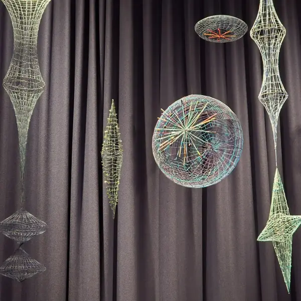  Fargerike og intrikate wireframe-skulpturer henger foran et mørkt sceneteppe. Skulpturene har geometriske og abstrakte former, inkludert sfærer og symmetriske design, og fremstår som belyste eller reflekterende.