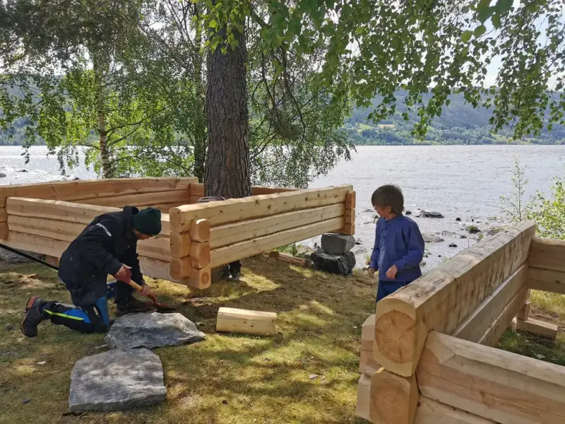 Et barn og en håndverker ved sandkasser av laft