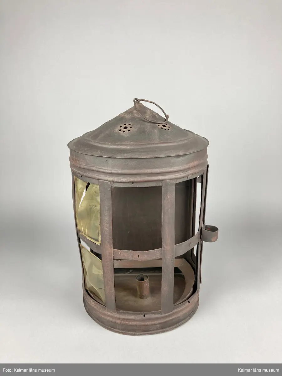 KLM 46905. Lykta. Av metall. Halvrund form med konisk överdel med genombrutet mönster. Plats för 9 rutor, varav två är försedda med hornskivor istället för glas. Dörr på sidan. På den platta baksidan finns fästen för upphängning. Målad i brun rostskyddsfärg.