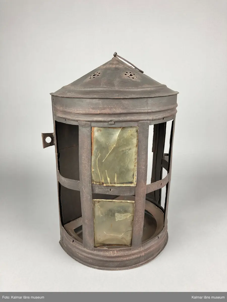 KLM 46905. Lykta. Av metall. Halvrund form med konisk överdel med genombrutet mönster. Plats för 9 rutor, varav två är försedda med hornskivor istället för glas. Dörr på sidan. På den platta baksidan finns fästen för upphängning. Målad i brun rostskyddsfärg.
