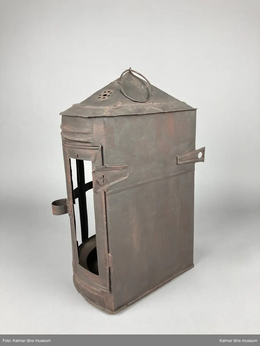 KLM 46905. Lykta. Av metall. Halvrund form med konisk överdel med genombrutet mönster. Plats för 9 rutor, varav två är försedda med hornskivor istället för glas. Dörr på sidan. På den platta baksidan finns fästen för upphängning. Målad i brun rostskyddsfärg.