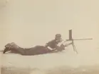 En man, soldat siktar med ett enpipigt skjutvapen på stativ. 
Text bak på foto: 