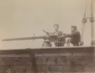 Två matroser på däck hanterar en kulspruta alternativt snabbskjutande kanon, tillverkad av Nordenfelts firma kring 1875 och framåt.