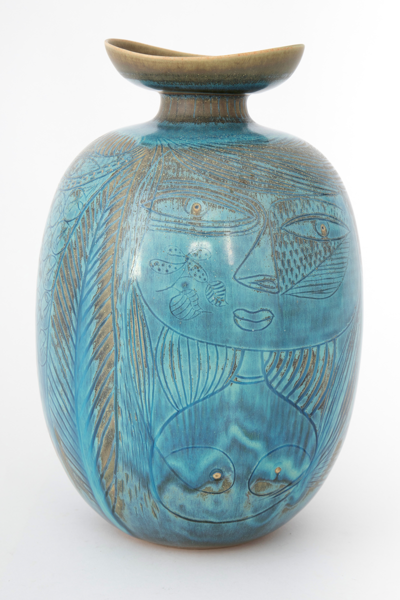 Krukke i steingods. Oval korpusform og kort innsnevret hals med vid, skålformet krage om munningen. Dekket med glasur i blå nyanser med overganger mot grågrønt. Innrisset dekor forestillende en kvinne i halvfigur, hus, tre, fisk samt en kvinne i helfigur mot en mønstret bakgrunn med ovaler og små ansikter.