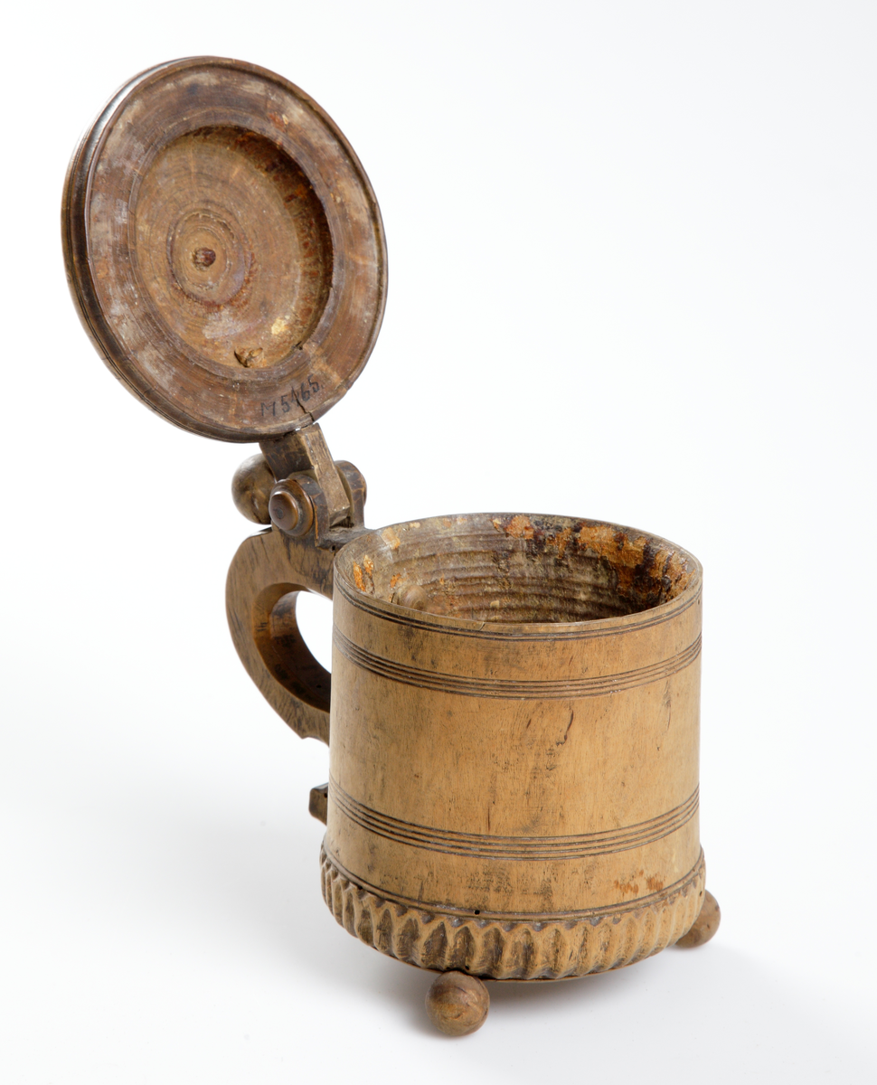 Stånka av trä, cylindriskt svarvad och med skuren dekor. Med gängat fällock och profilerat handtag. Stående på tre kulfötter.

Inskrivet i huvudkatalog 1933.