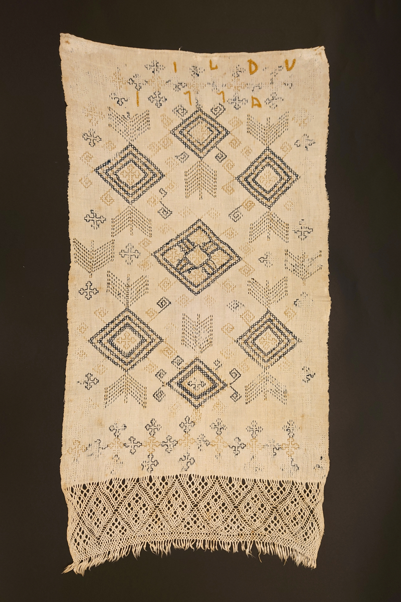 Julehandkle i grov lin med 15 cm brei firflettingsbord i nedre enden. Over heile handkledet er det brodert mønster i holbeinsting i blått og lys gulbrunt ullgarn. Enkelte plassar er ulltråden borte, slik at det står att berre merke etter den. Øverst på handkledet er det brodert 1774 (?) og bokstavane ILDV (?) i kjedesting. Desse er brodert med eit tjukkare ullgarn i gult.
Handkledet er falda i øvrekanten. og det er jarekantar i sidene.
I kanten øverst er det påsydd tre små hemper for å henga opp handkledet. Fint stoppa i endane øverst.