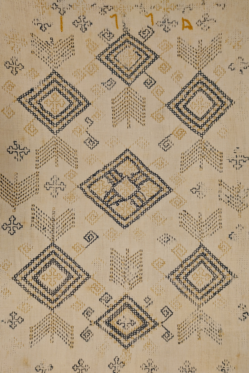 Julehandkle i grov lin med 15 cm brei firflettingsbord i nedre enden. Over heile handkledet er det brodert mønster i holbeinsting i blått og lys gulbrunt ullgarn. Enkelte plassar er ulltråden borte, slik at det står att berre merke etter den. Øverst på handkledet er det brodert 1774 (?) og bokstavane ILDV (?) i kjedesting. Desse er brodert med eit tjukkare ullgarn i gult.
Handkledet er falda i øvrekanten. og det er jarekantar i sidene.
I kanten øverst er det påsydd tre små hemper for å henga opp handkledet. Fint stoppa i endane øverst.