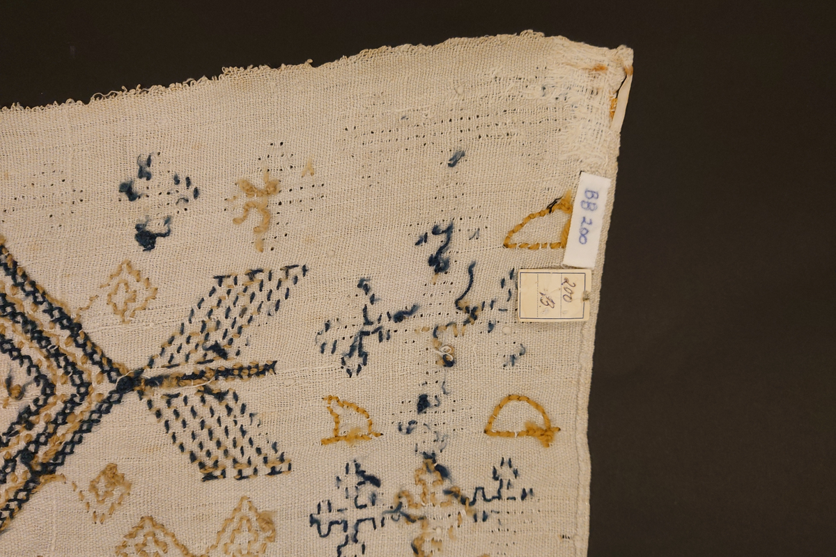 Julehandkle i grov lin med 15 cm brei firflettingsbord i nedre enden. Over heile handkledet er det brodert mønster i holbeinsting i blått og lys gulbrunt ullgarn. Enkelte plassar er ulltråden borte, slik at det står att berre merke etter den. Øverst på handkledet er det brodert 1774 (?) og bokstavane ILDV (?) i kjedesting. Desse er brodert med eit tjukkare ullgarn i gult.
Handkledet er falda i øvrekanten. og det er jarekantar i sidene.
I kanten øverst er det påsydd tre små hemper for å henga opp handkledet. Fint stoppa i endane øverst.