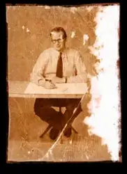 En manlig modell sitter vid ett bord och arbetar. Ateljébild