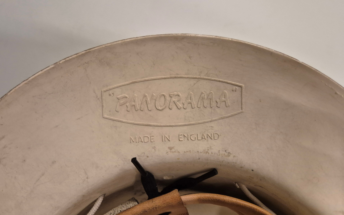 Hjelm i hvit plast med brem. Lampefeste foran på hjelmen. Innmaten utgjøres av lær og bomullsbånd, og hjelmen har et ca 1 cm bredt bomullsbånd til feste under haka. Alt er festet i en hvit rund snor som går rundt hele hjelmen.