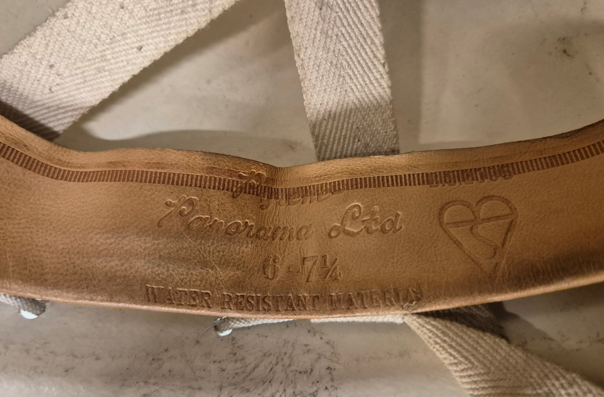 Hjelm i hvit plast med brem. Lampefeste foran på hjelmen. Innmaten utgjøres av lær og bomullsbånd, og hjelmen har et ca 1 cm bredt bomullsbånd til feste under haka. Alt er festet i en hvit rund snor som går rundt hele hjelmen.