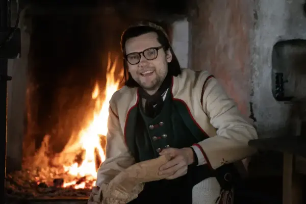 En mann i folkedrakt fra Numedal sitter foran peisen i Grøslistua på Norsk Folkemuseum. 