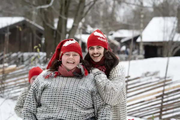 En mann og en dame iført nisseluer på Norsk Folkemuseum. Det er vinter og snø. 