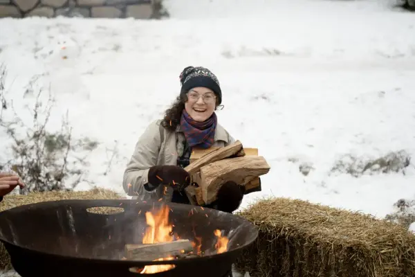 En kvinne legger på mer ved i bålpanna. 